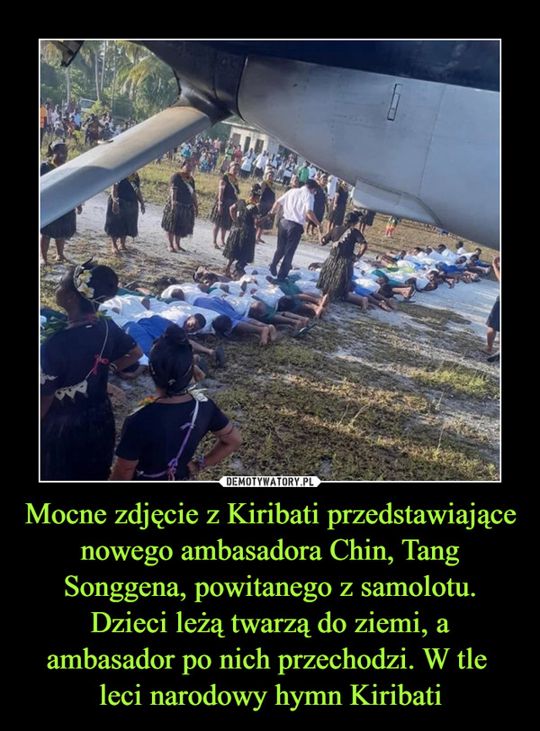 Mocne zdjęcie z Kiribati przedstawiające nowego ambasadora Chin, Tang Songgena, powitanego z samolotu. Dzieci leżą twarzą do ziemi, a ambasador po nich przechodzi. W tle 
leci narodowy hymn Kiribati